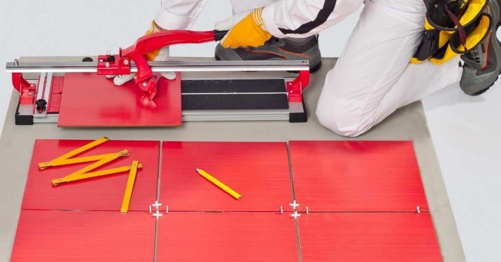 Person cutting red ceramic tile with manual tile cutter