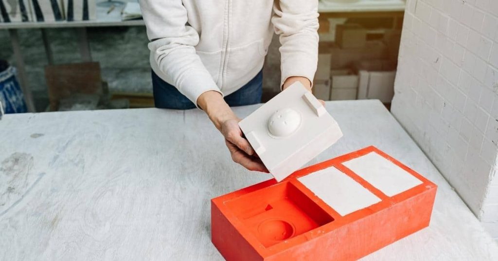 Person holding plaster mold above red tray with plaster samples