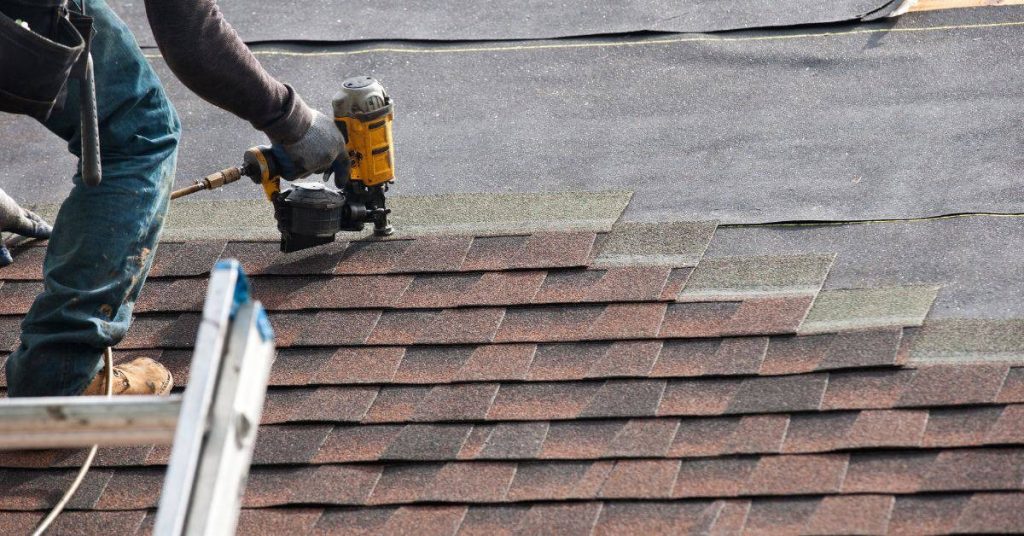 Person installing asphalt shingles on roof with nail gun