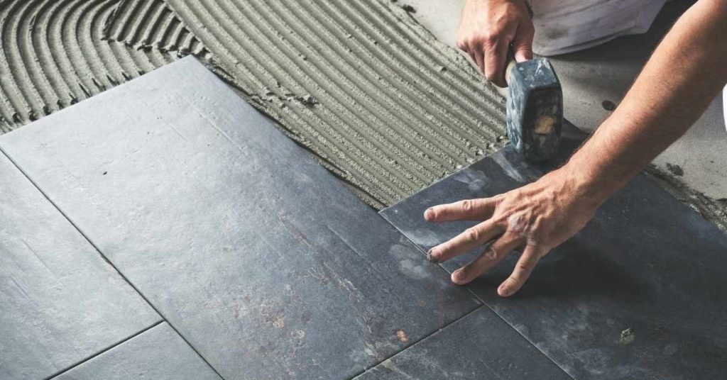 Person installing dark ceramic floor tiles with hammer and mortar