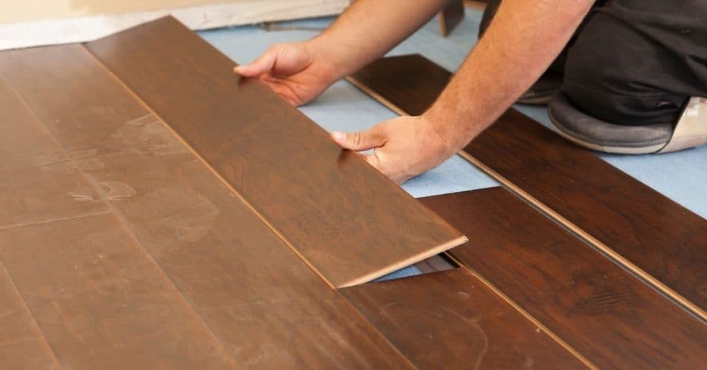 Person installing dark laminate flooring indoors