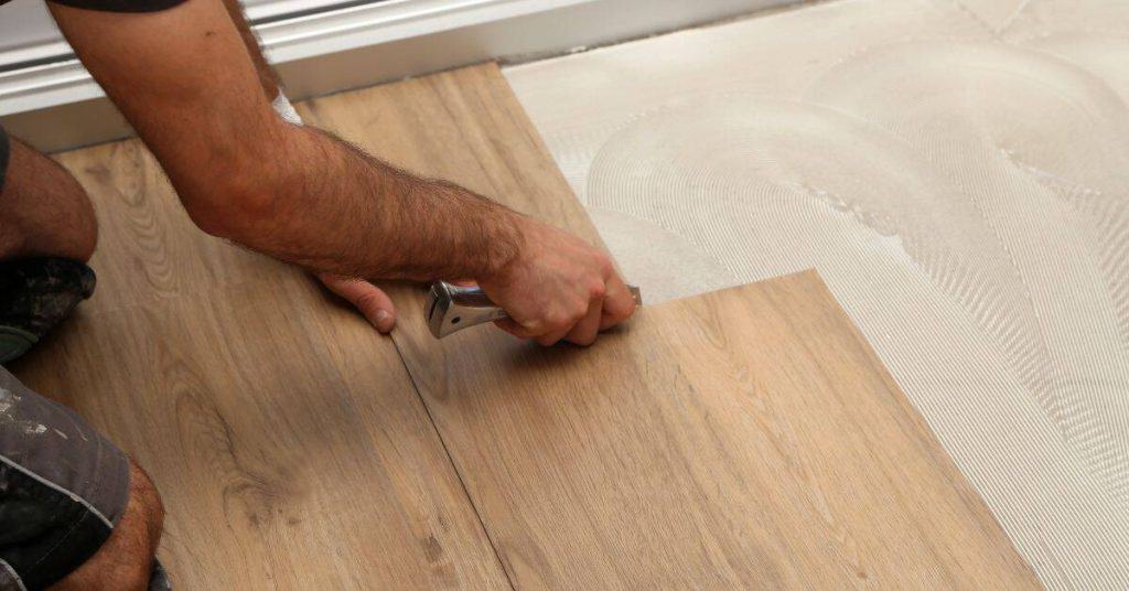 Person installing laminate wood flooring by hand