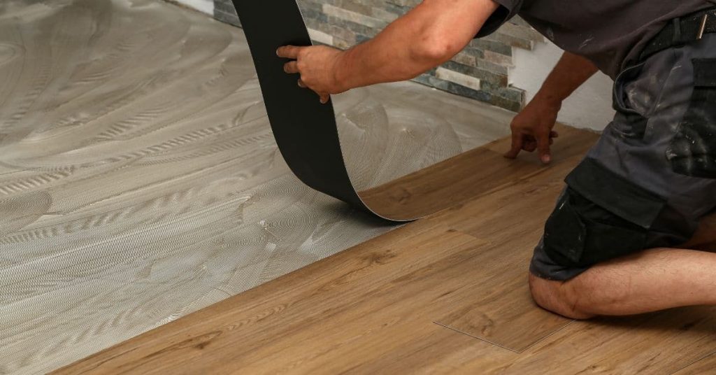 Person installing vinyl plank flooring over adhesive