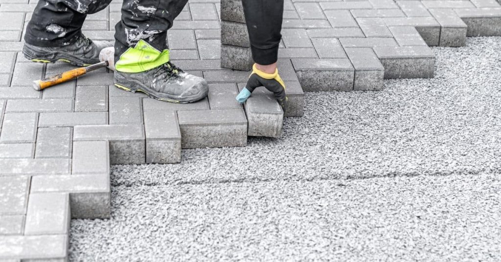 Person laying concrete paving blocks on gravel base