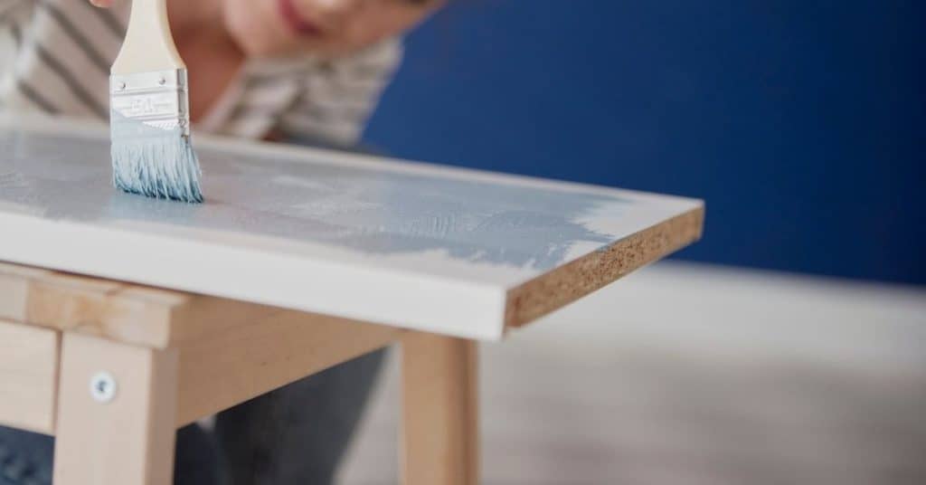Person painting edge of wooden board with brush