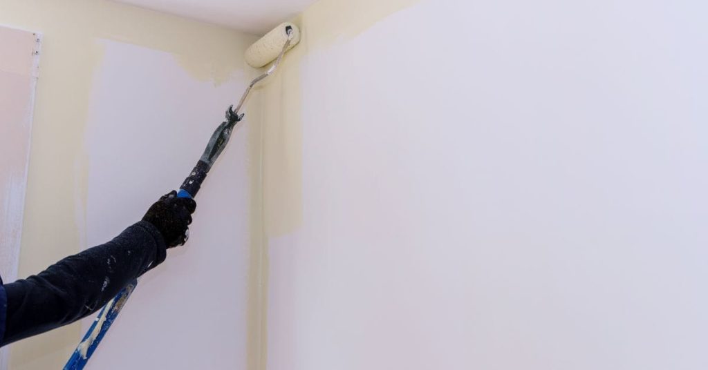 Person painting interior wall with roller near ceiling corner