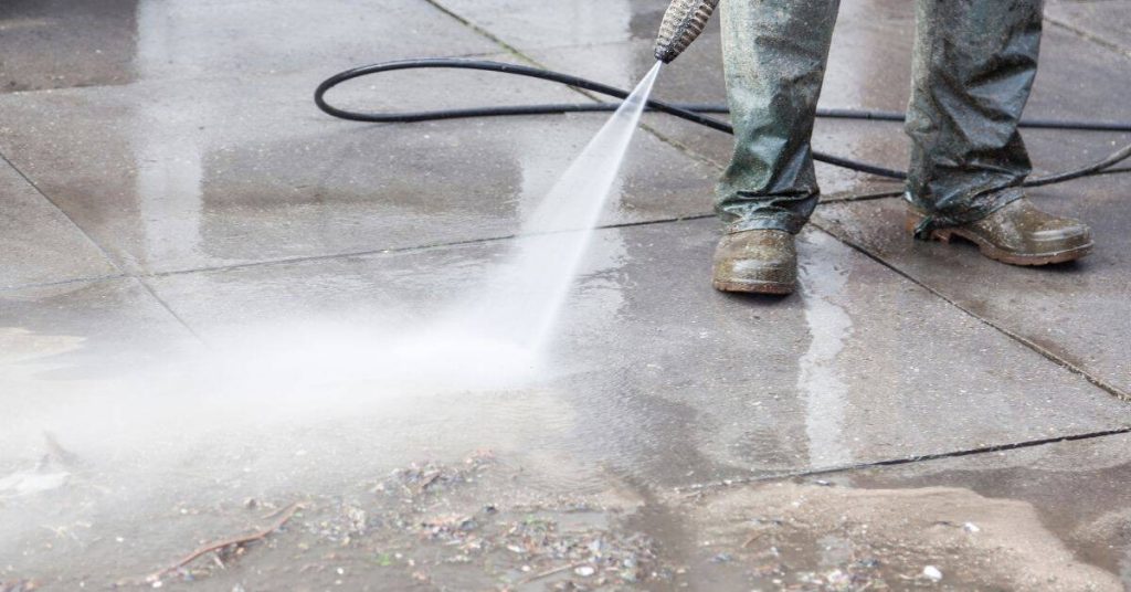 Person pressure washing smooth concrete patio surface