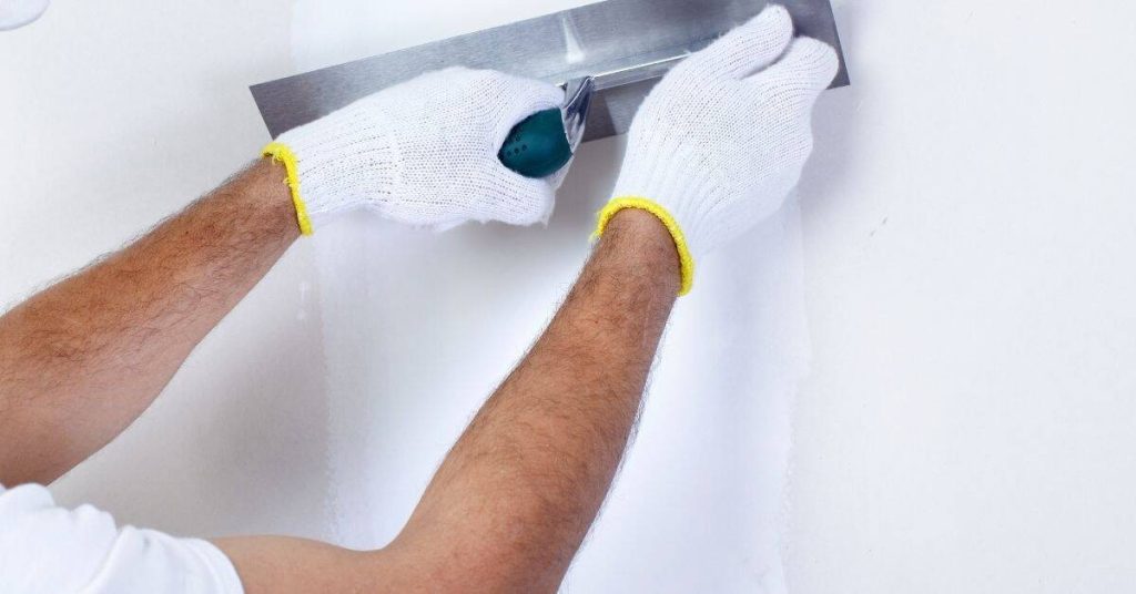 Person smoothing white plaster on wall with metal trowel