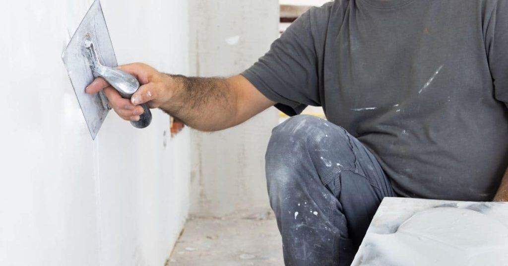 person smoothing white plaster on wall with trowel