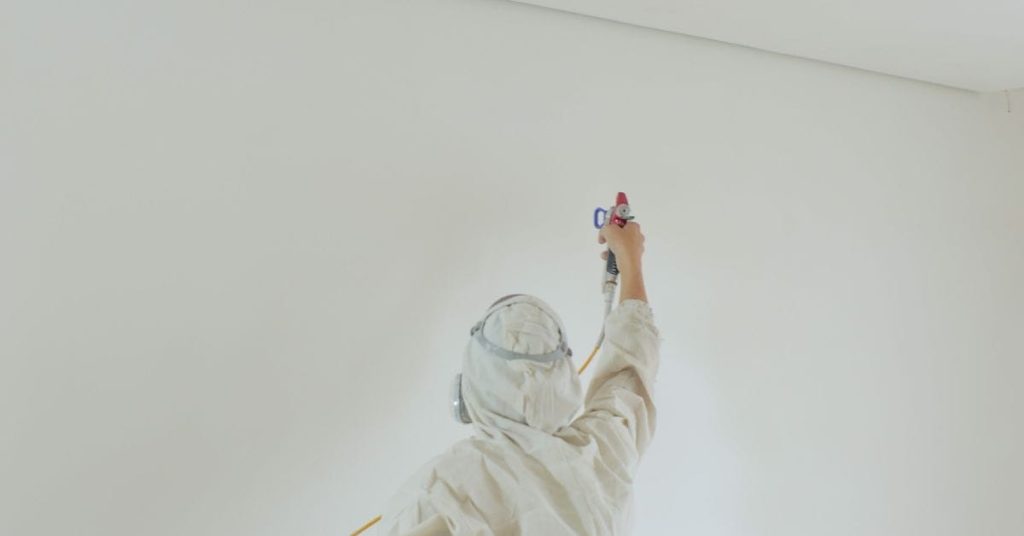 Person spraying paint on white interior wall wearing protective gear
