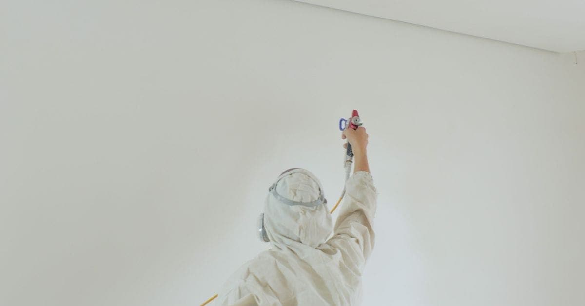 Person spraying paint on white interior wall wearing protective suit