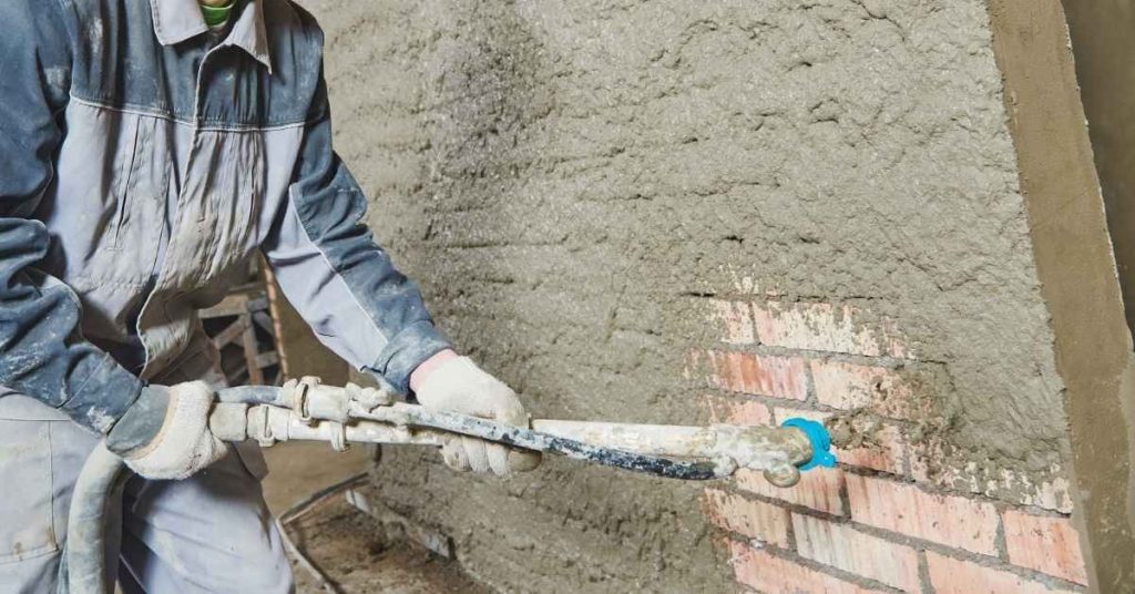 Person spraying wet stucco on brick wall