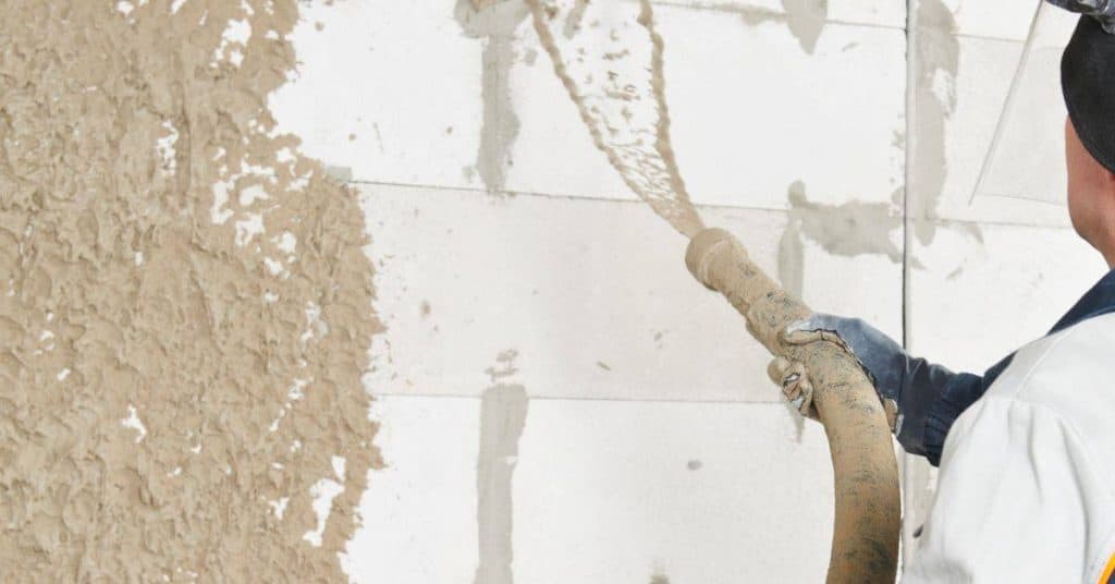 Person spraying wet stucco onto a wall with hose