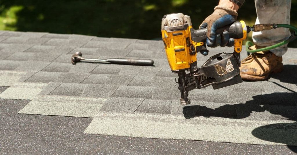 Person using pneumatic nail gun on asphalt shingle roof
