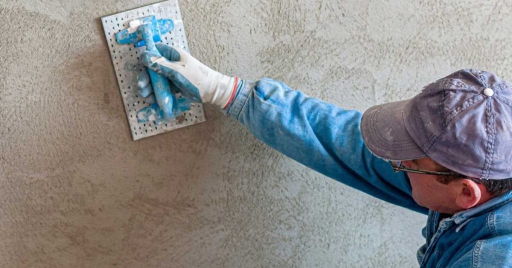 person wearing cap and gloves applying plaster with float