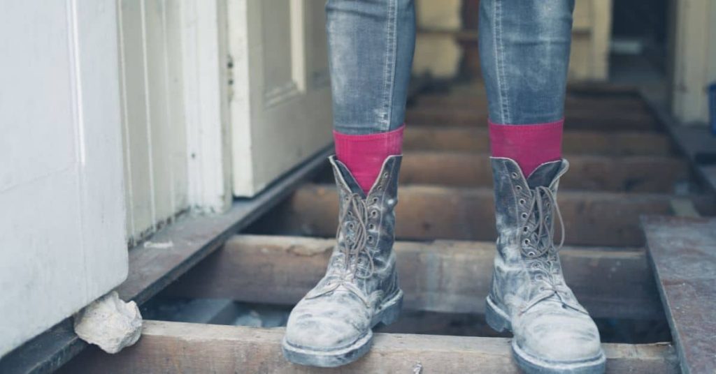 Person wearing dusty work boots standing on exposed wooden floor joists