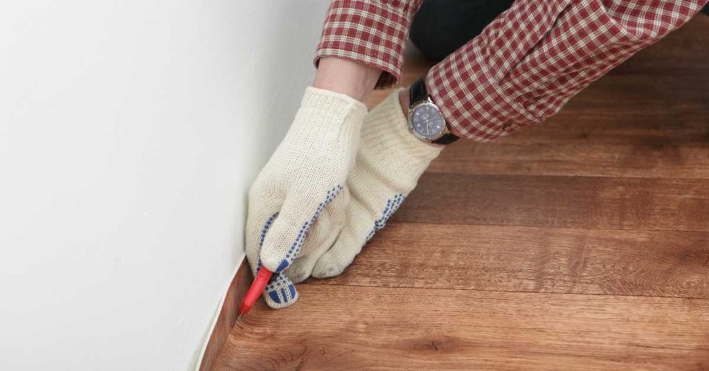 Person wearing gloves marking wood flooring edge by wall