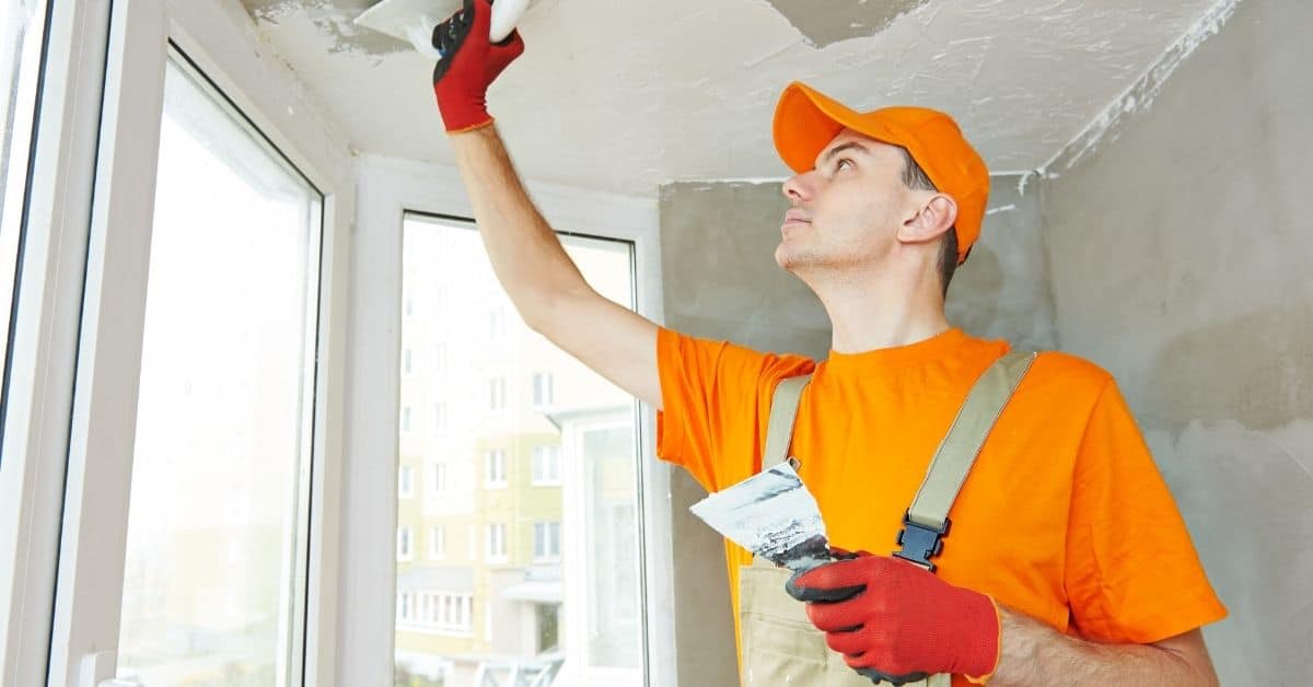 Worker applying plaster to ceiling with putty knife