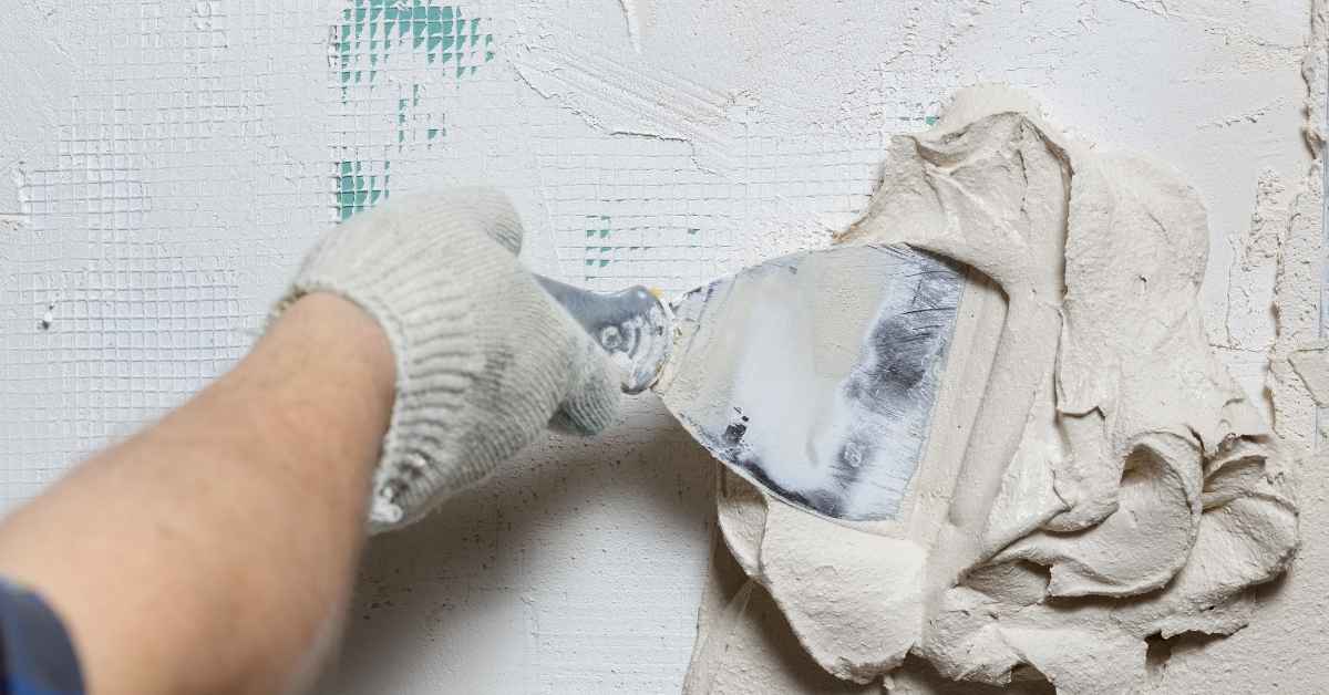 Hand with glove applying plaster onto mesh with putty knife