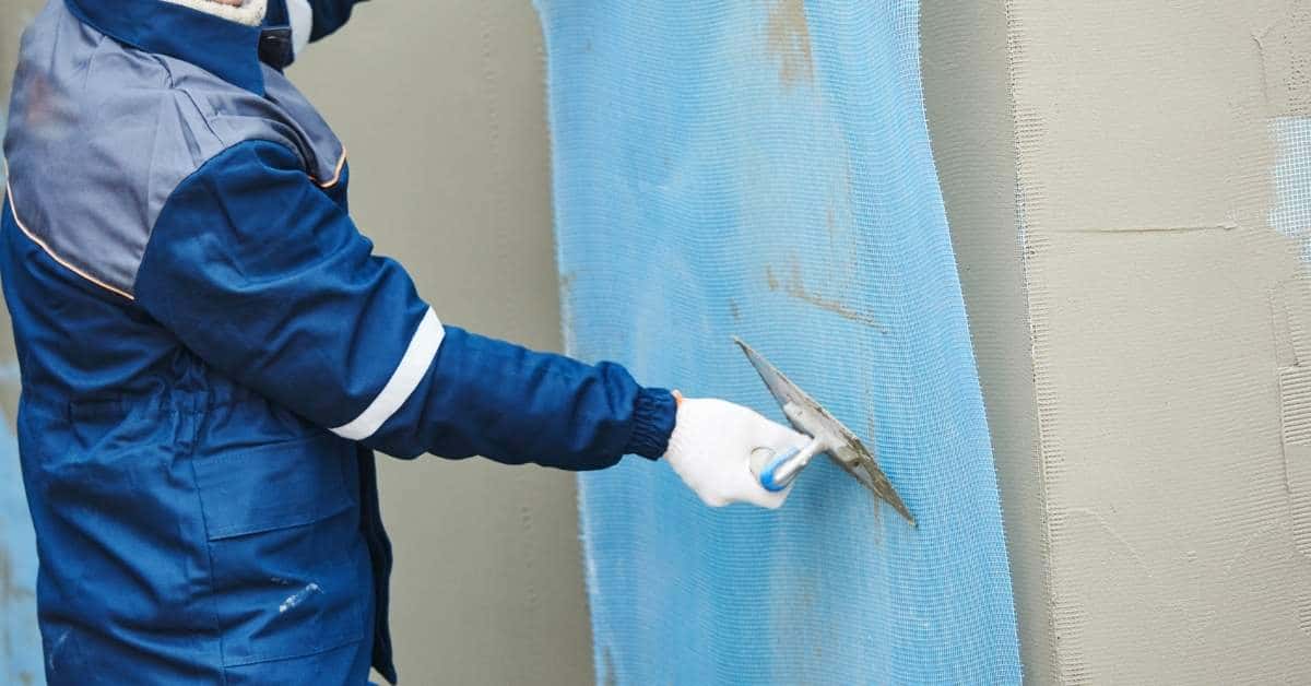 Worker applying plaster over blue reinforcing mesh on wall