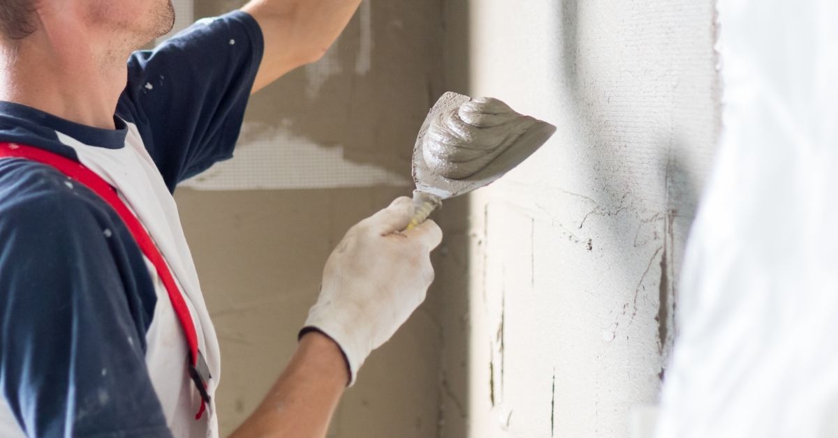 Person applying plaster mix to wall with trowel