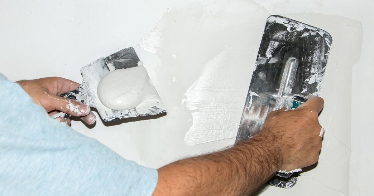 Hand applying white plaster on wall with trowel and hawk