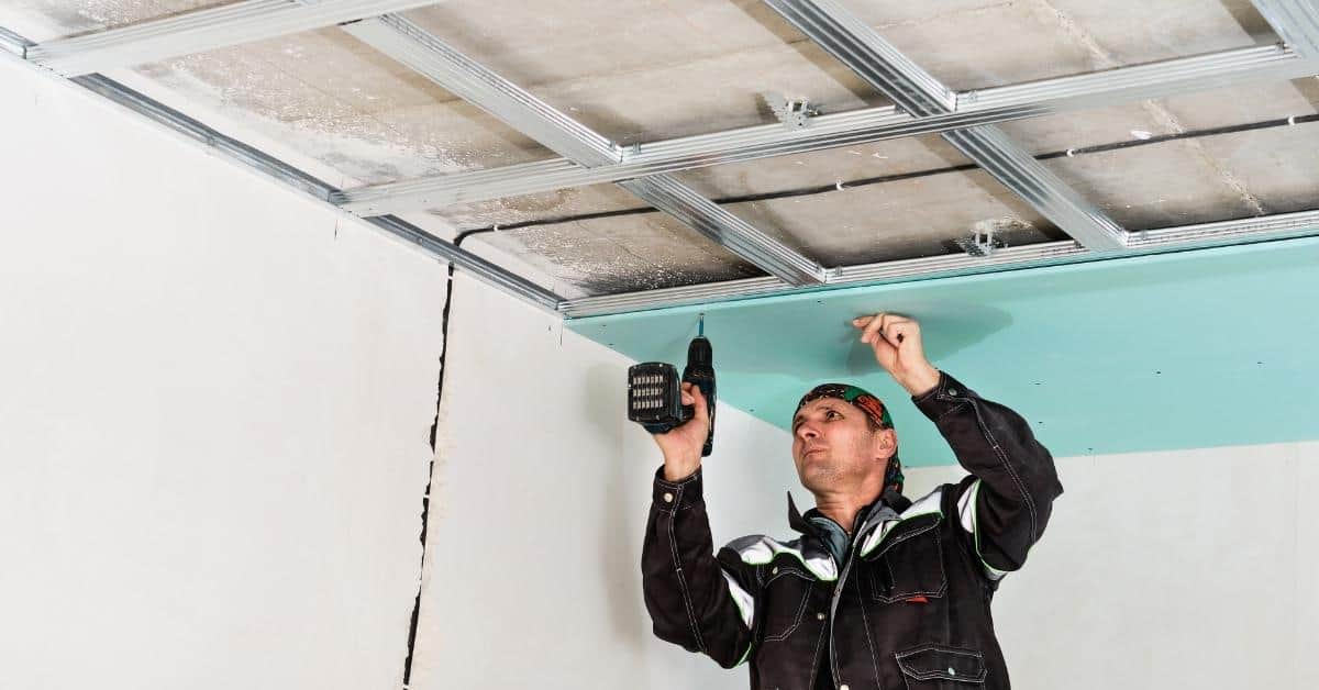 Worker installing blueboard ceiling panel with cordless drill
