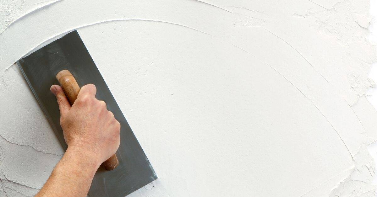 Hand smoothing white plaster on wall with trowel