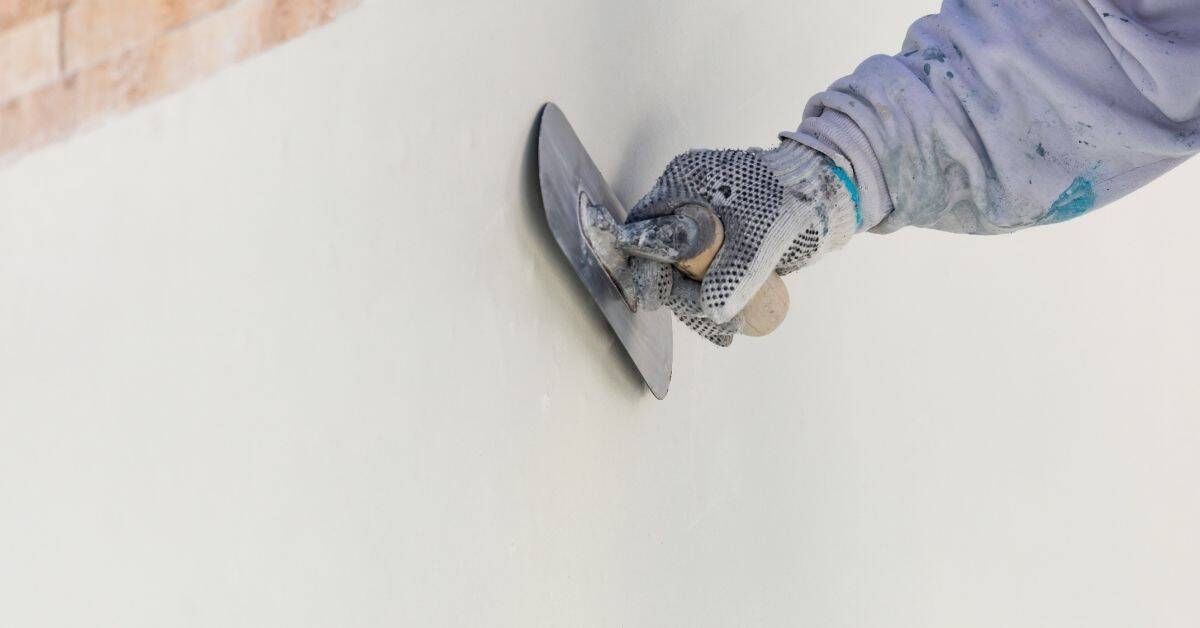 Hand with glove troweling smooth plaster on wall