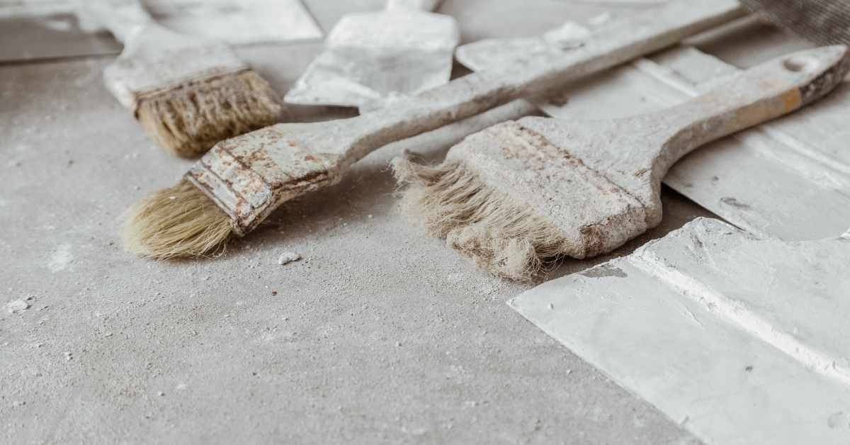 Three used paint brushes covered in plaster dust on concrete surface