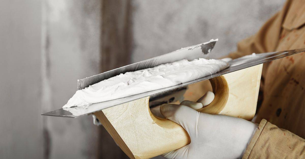Hand holding trowel with white plaster ready for application