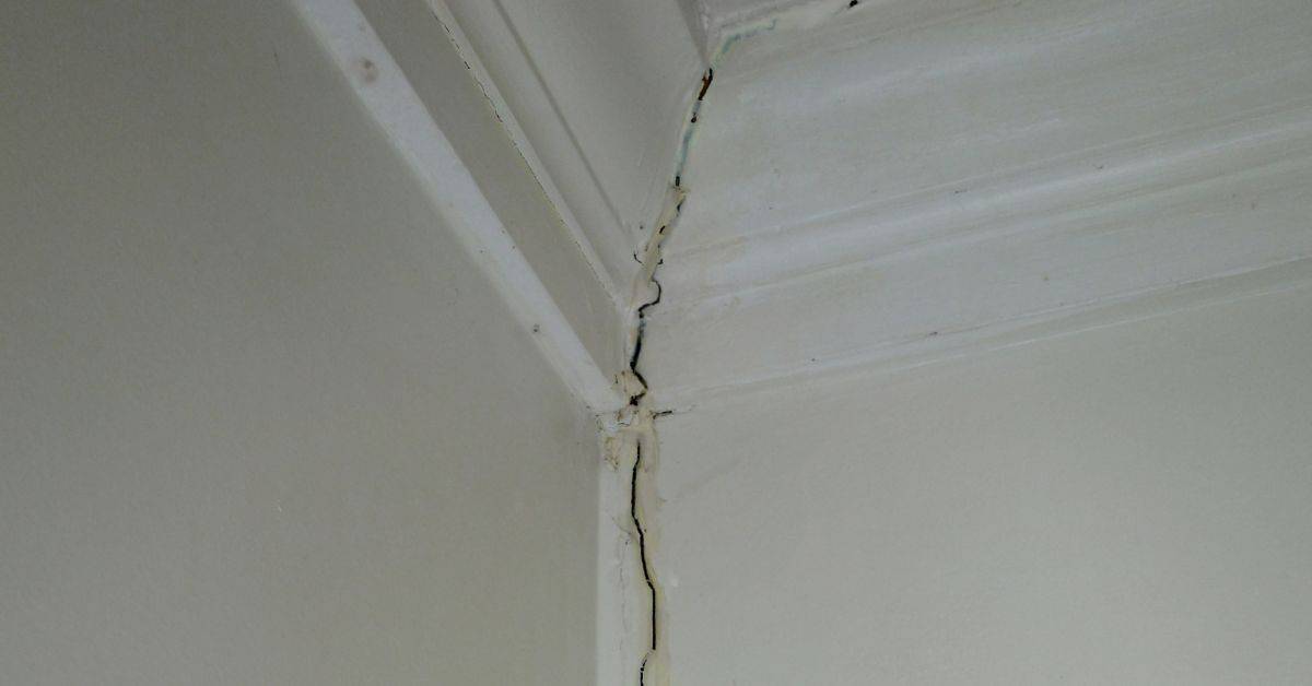 Closeup of crack in plaster wall corner near ceiling molding