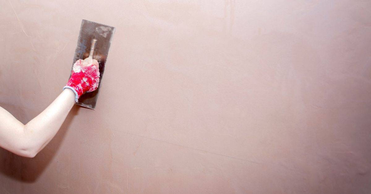 Person smoothing wall plaster using trowel and red glove