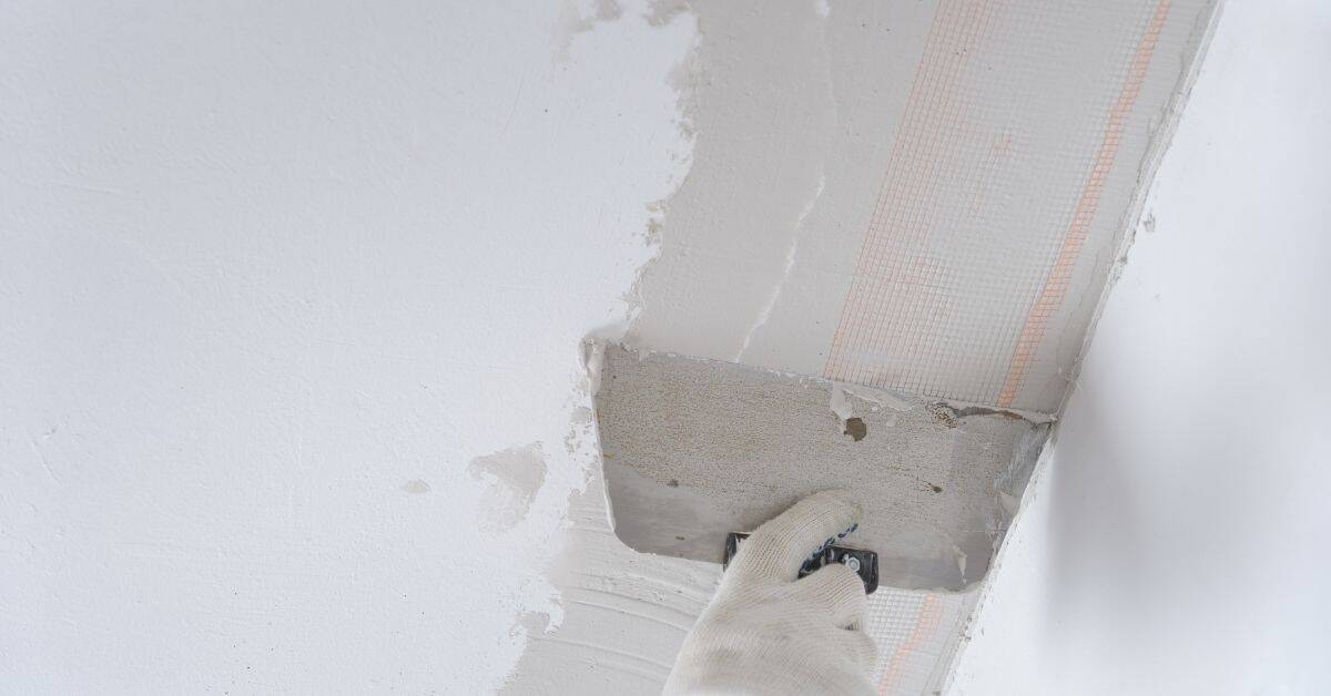 Hand applying plaster to ceiling corner with trowel