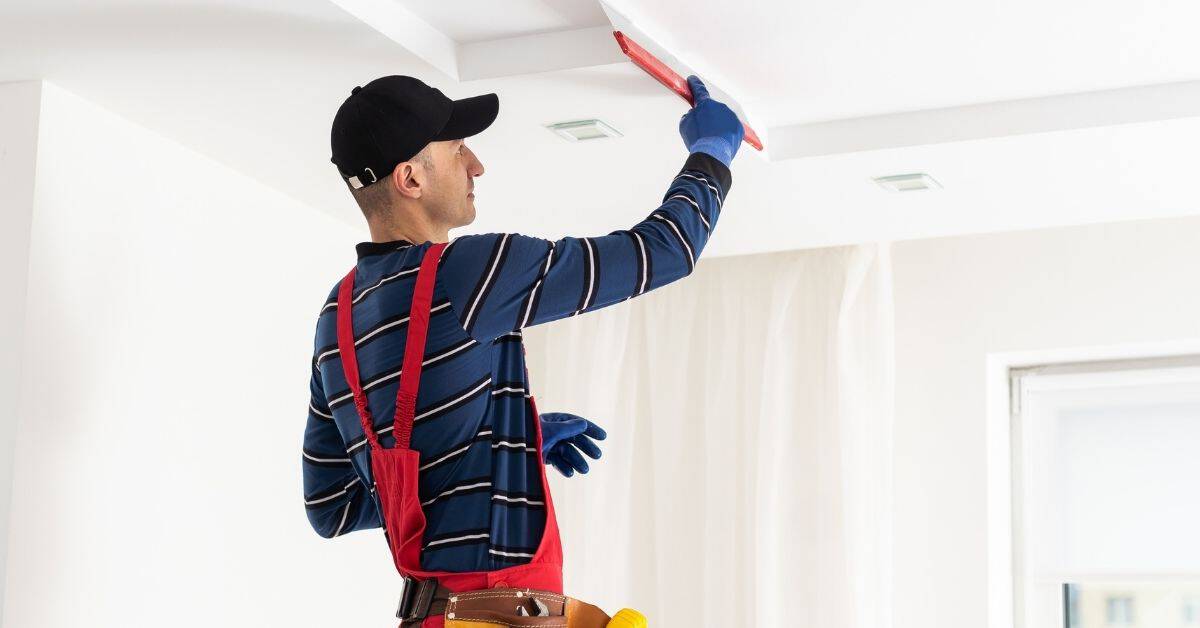 man plastering a white ceiling with red trowel