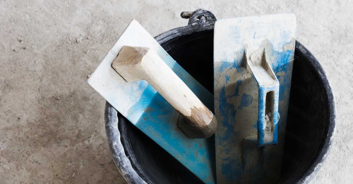 Two plastering floats inside a black bucket on concrete floor