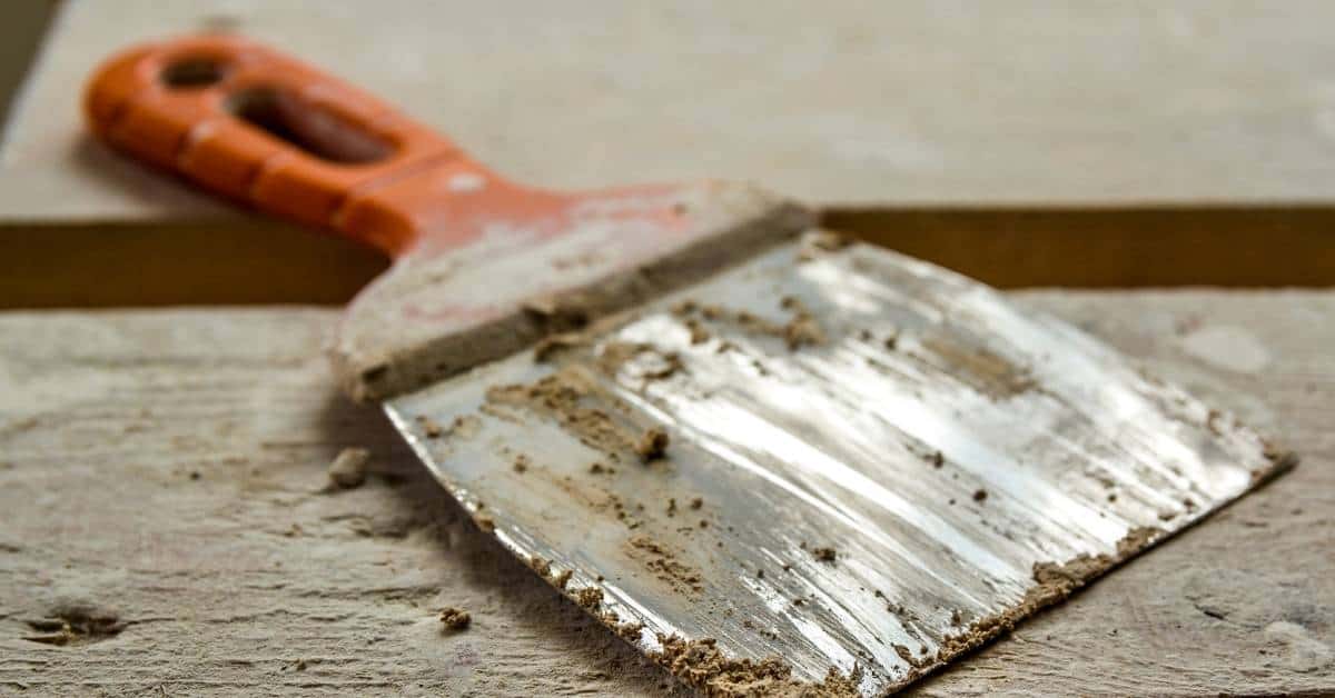 putty knife with dried plaster on blade and wooden surface