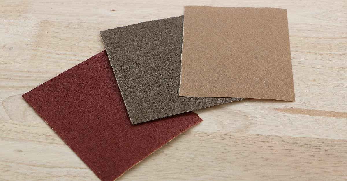 Three sheets of sandpaper in different grits on wood surface