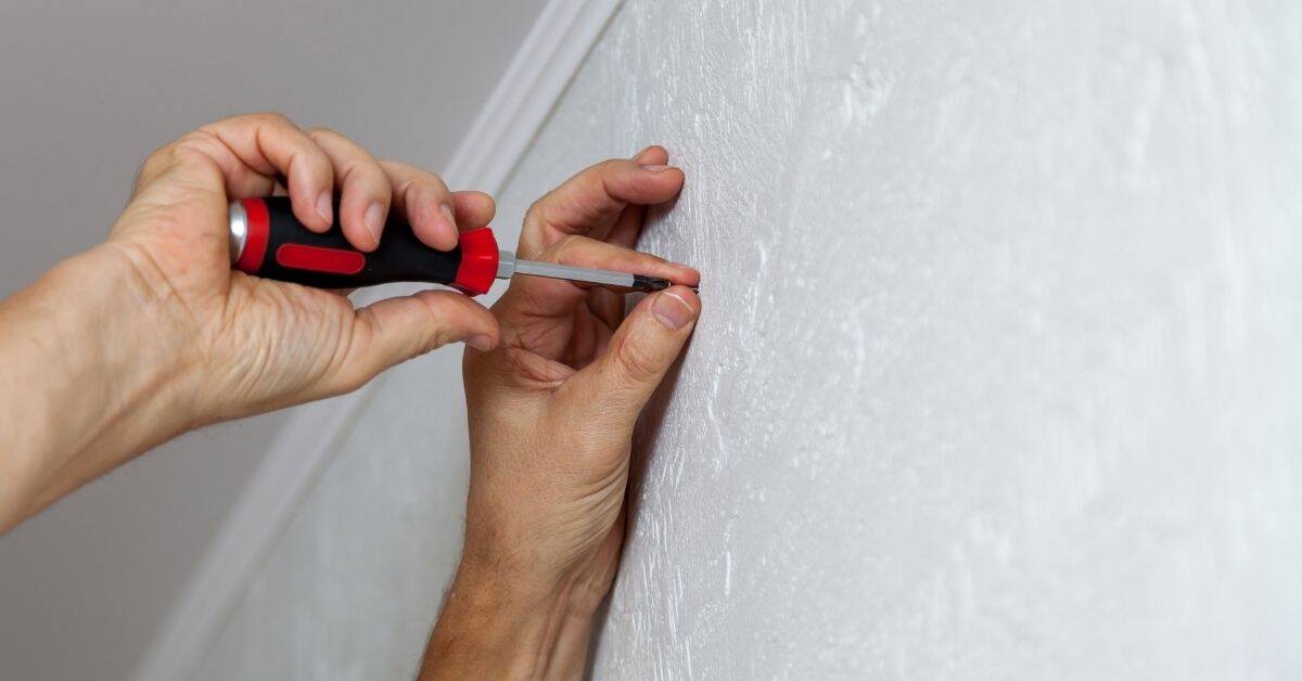 Hands using screwdriver inserting screw into plaster wall