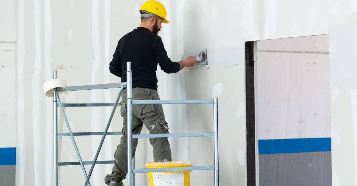 Worker wearing yellow helmet applying plaster on drywall