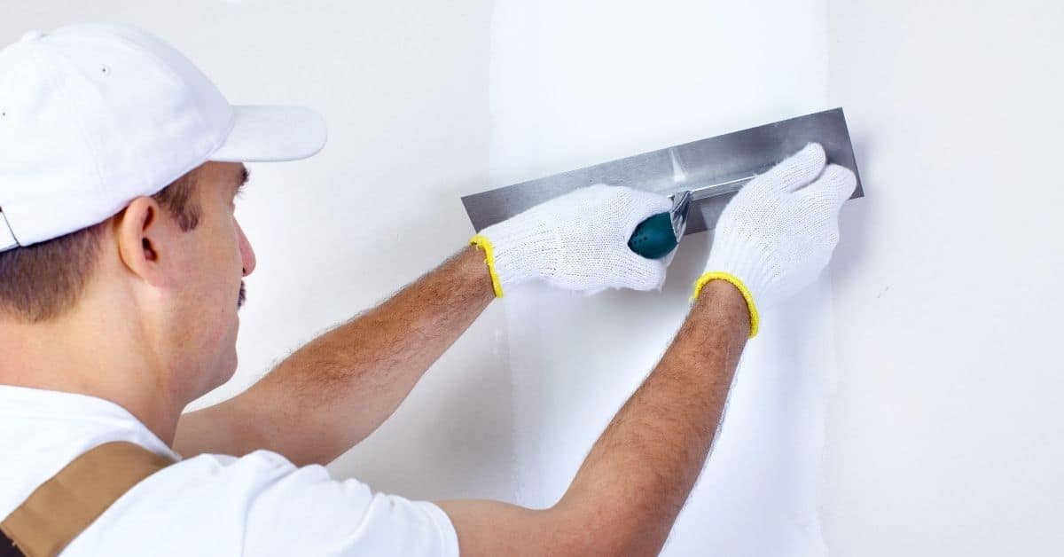 Worker smoothing white plaster on wall with trowel