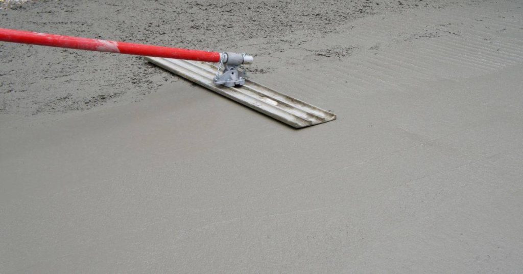Red-handled tool smoothing wet concrete surface