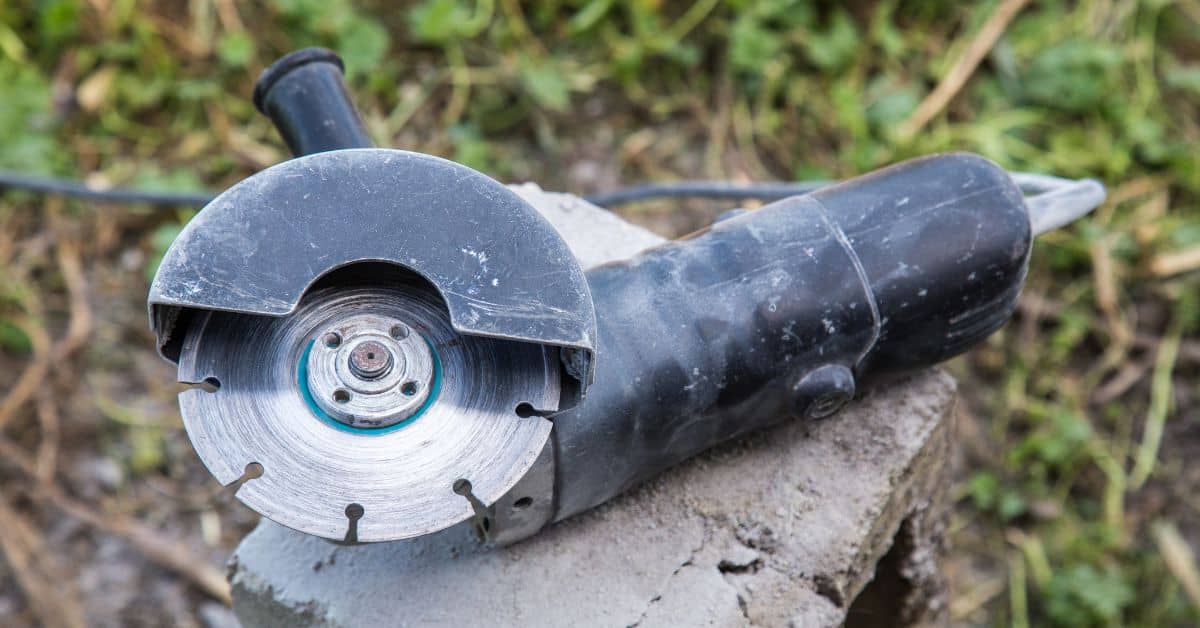 Black angle grinder resting on concrete block outdoors