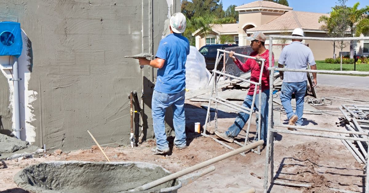 Workers applying stucco to exterior wall with tools