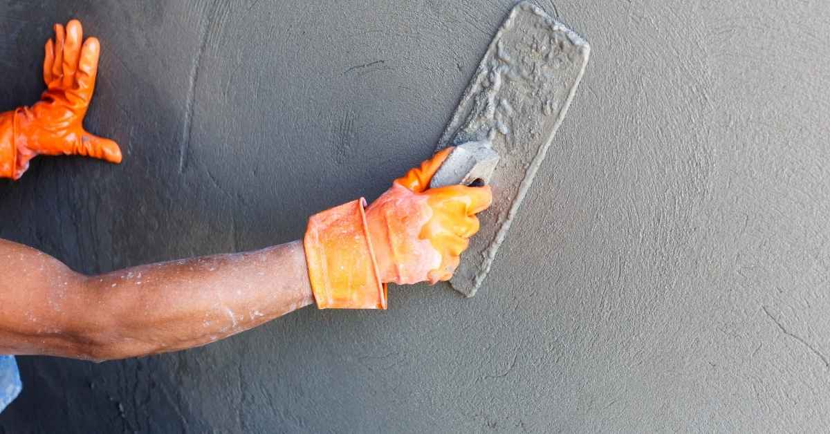 Person wearing orange gloves applying stucco with trowel