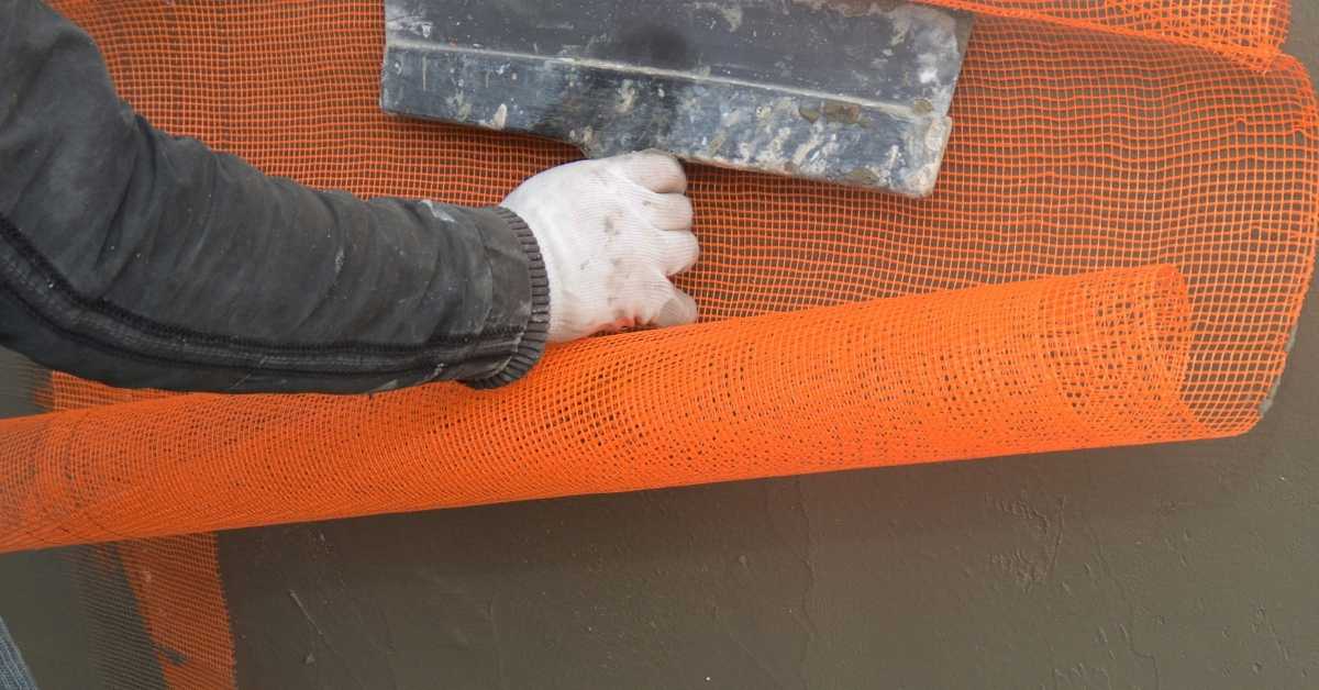 Hand applying orange fiberglass mesh over stucco surface