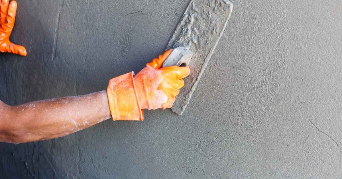 Hand wearing orange glove smoothing wet stucco with trowel