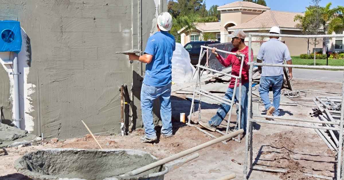 Three workers preparing and applying stucco on exterior wall