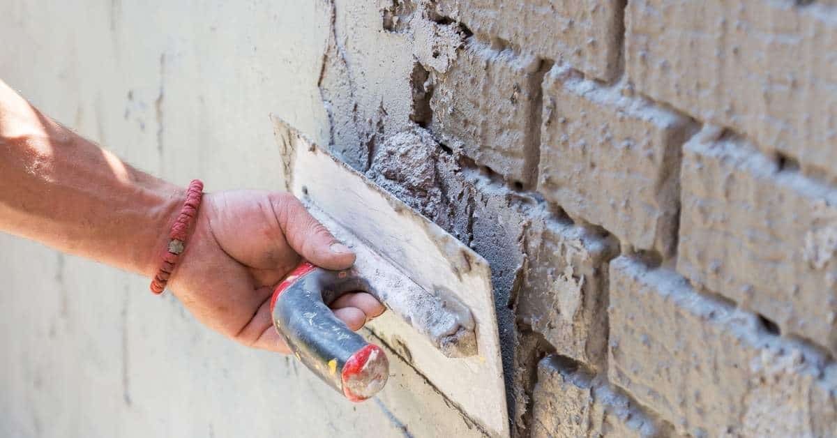 Hand applying stucco with trowel on brick wall