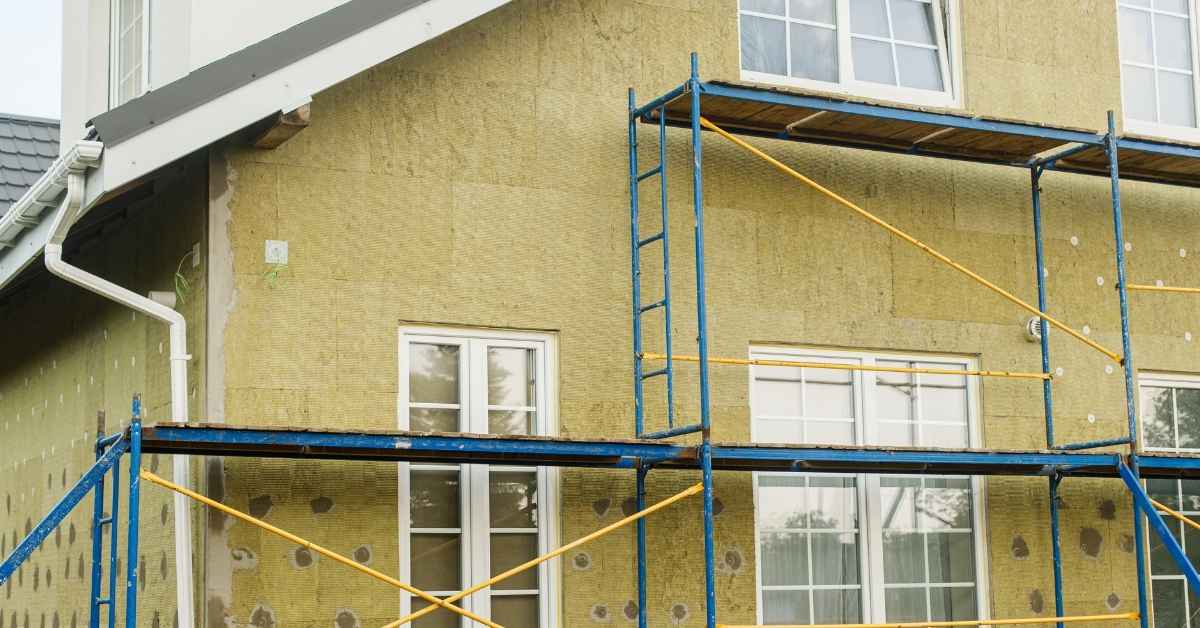 Exterior wall with insulation and scaffolding near double-hung windows